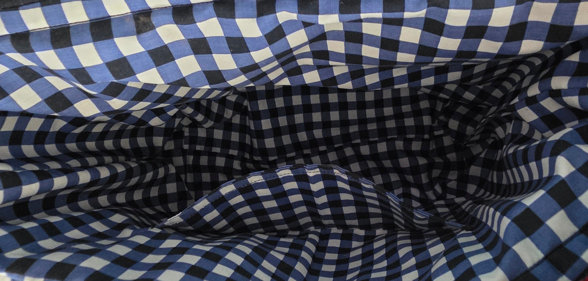A close-up of a hand holding open a fabric pouch or bag with a blue, white, and black gingham checkered pattern.