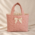 A small pink patterned fabric tote bag with cream-colored handles and a matching bow on the front.
