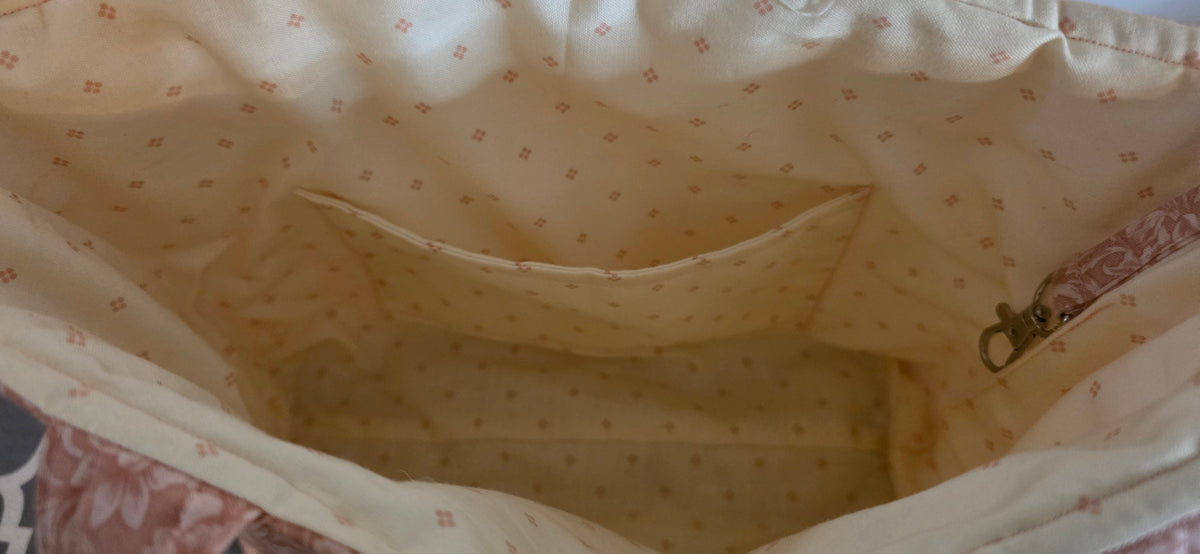 Close-up view of the interior lining of a fabric bag or pouch, showing a cream-colored fabric with a small pink floral pattern with interior pocket.