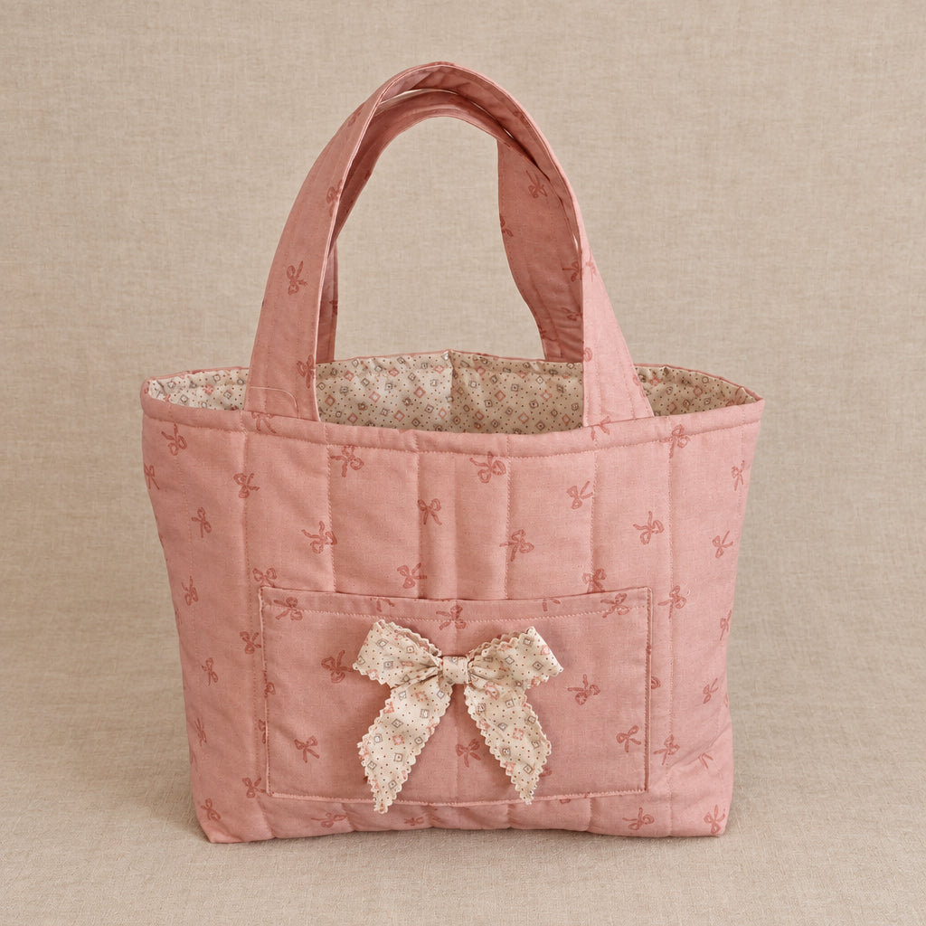 A small quilted pink fabric tote bag with a bow on the front.