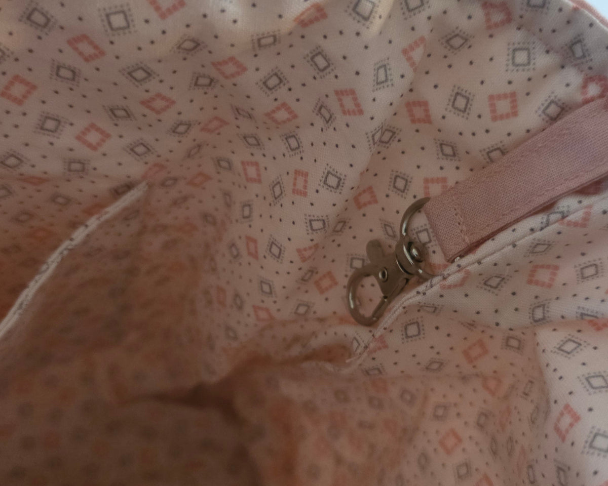 Close-up of the interior lining of a soft bag or pouch, showing a light pink fabric with a small repeating geometric diamond pattern in muted red and gray and metal clasp.