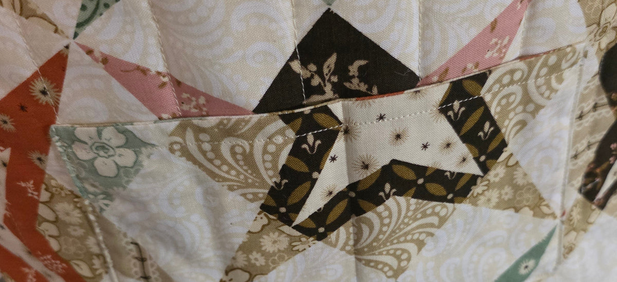 A close-up of a handmade quilted fabric bag or pouch with a geometric patchwork design.