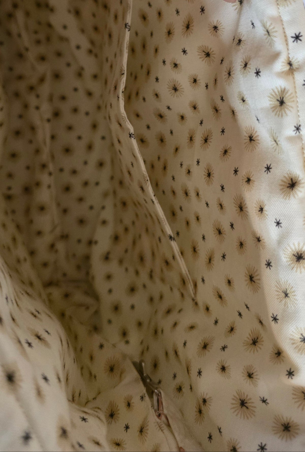 Close-up of a beige fabric with a black star and sunburst pattern, showing a hand pulling out a side pocket.
