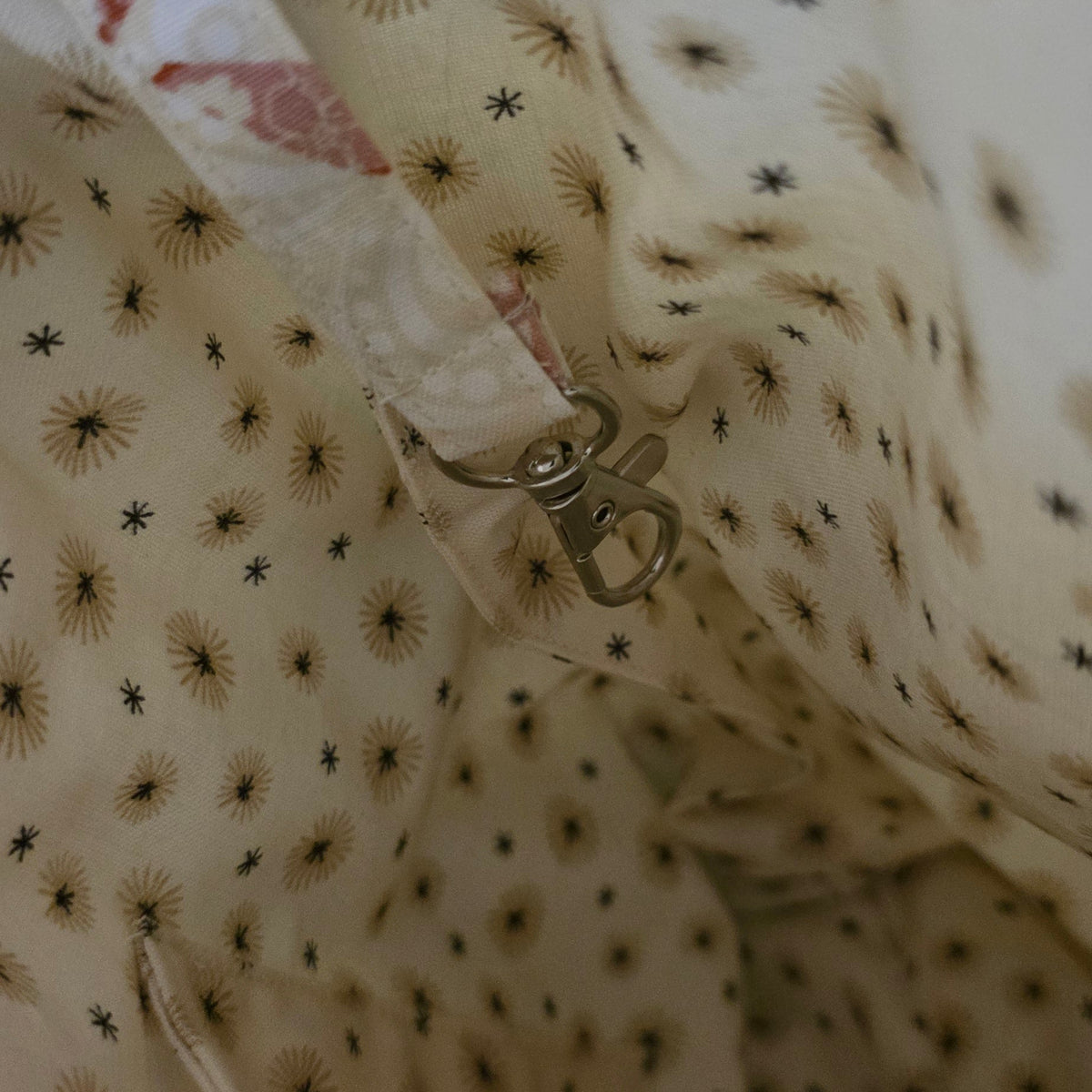 Close-up of a beige fabric bag or pouch with a repeating black starburst pattern, showing the interior lining and a small metal clasp