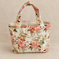 A small fabric tote bag with a floral print pattern, featuring two top handles and a quilted stitched texture, on a clean warm linen background