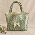A small fabric tote bag with a green and white geometric pattern, dual top handles, and a cream-colored bow on the front.