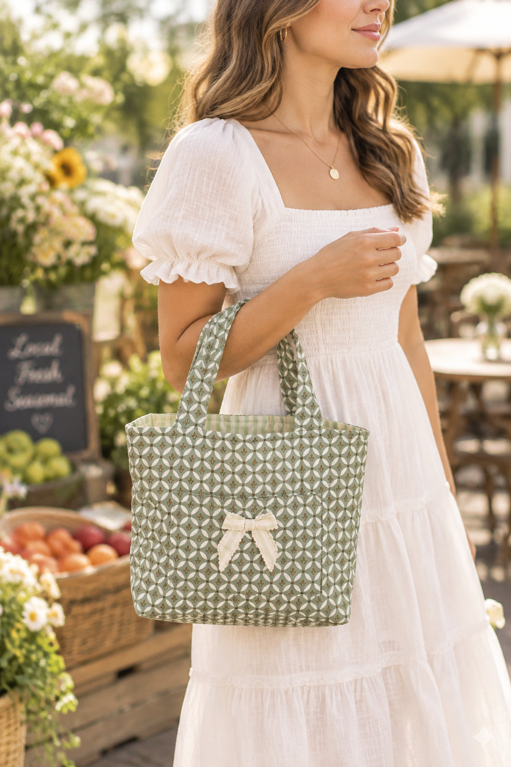 A small fabric tote bag with a green and white geometric pattern, dual top handles, and a cream-colored bow on the front.