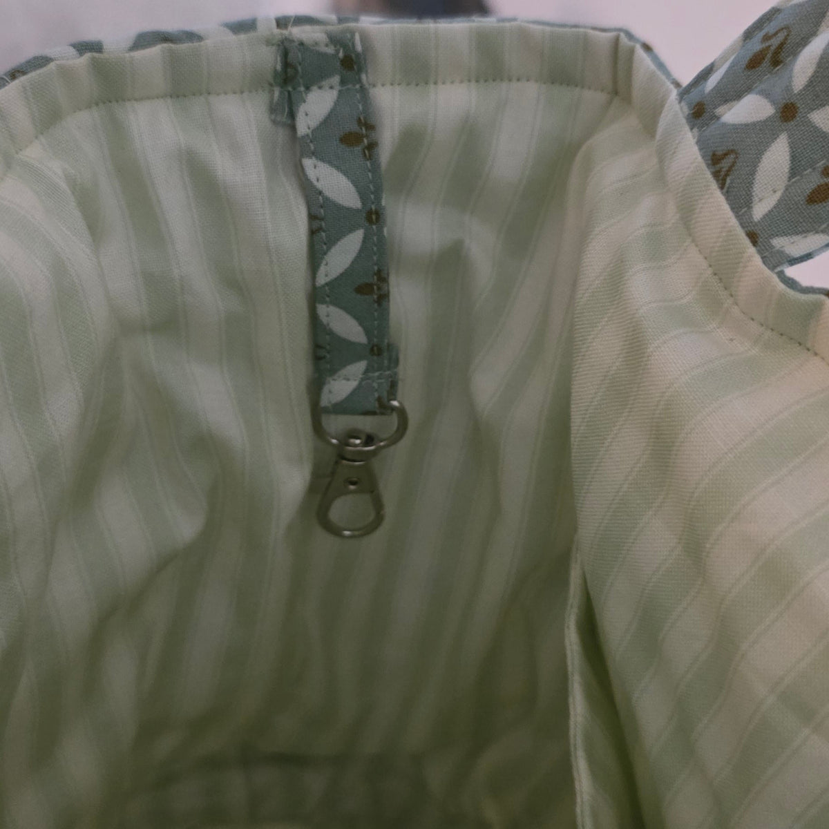 Close-up of the interior of a light green and white striped fabric bag, showing a patterned green zipper pull and a metal zipper tab.
